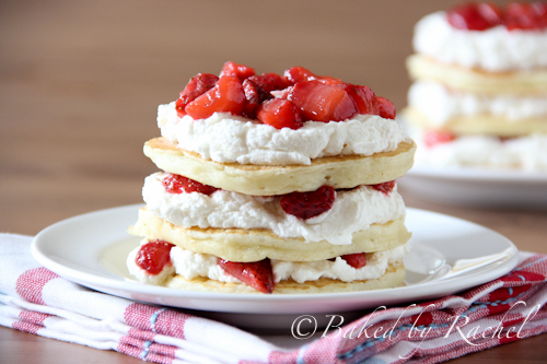 Front view of three pancakes layered with whipped cream and strawberries on small white plate.