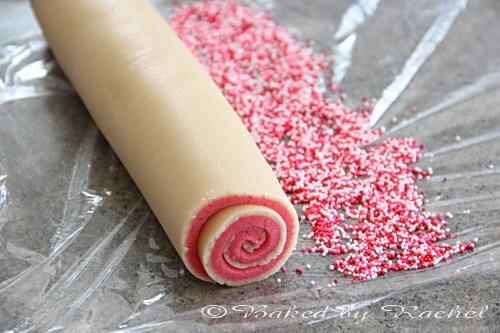 A log of cookie dough being rolled in sprinkles.