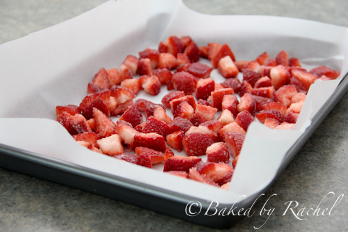 Baking pan lined with parchment containing strawberries before roasting.