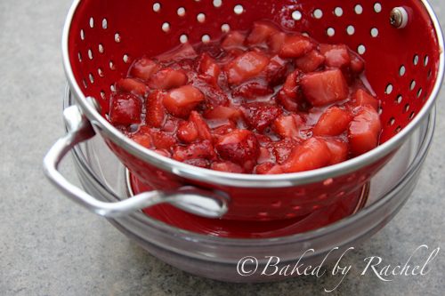 Roasted strawberries in red metal colander draining into clear glass bowl.