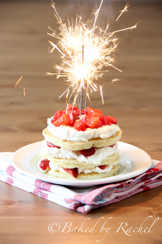 Pancakes, whipped cream, and strawberries topped with burning sparkler.